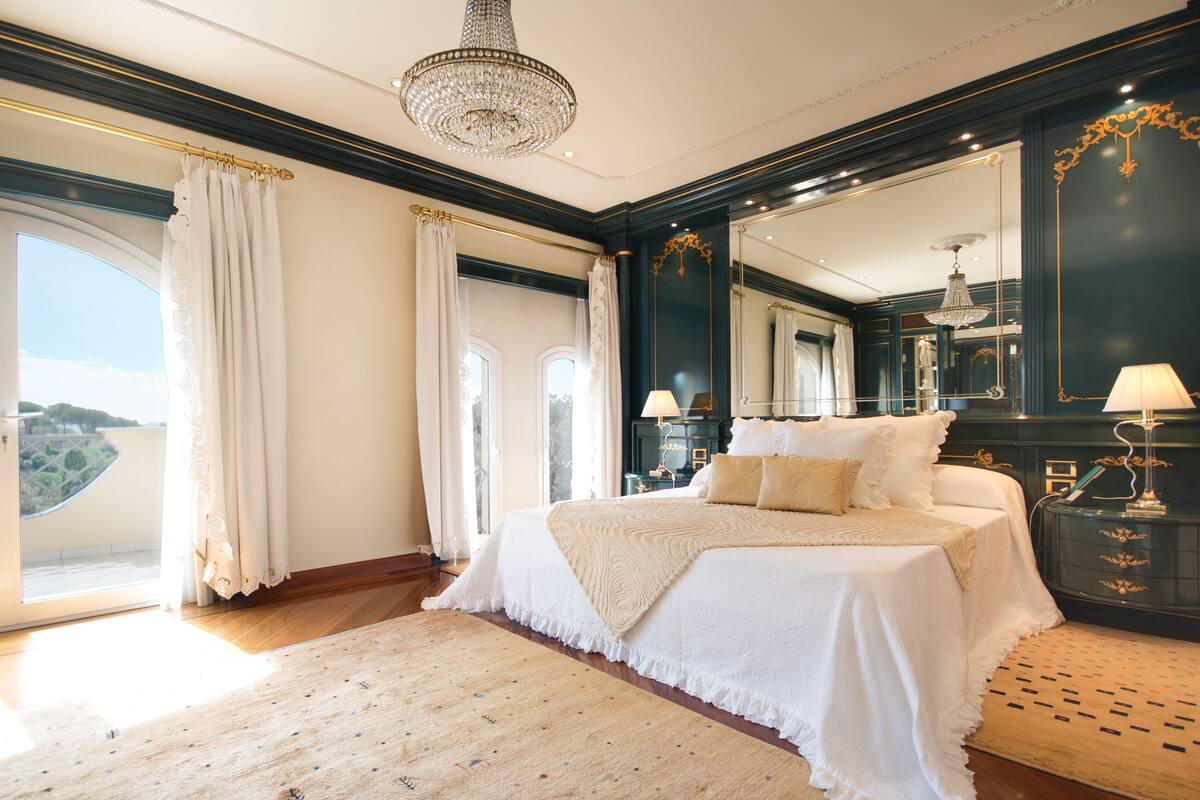 Une chambre à coucher luxueuse, dotée d’un grand lit, d’un lustre et offrant une vue sur l’extérieur.