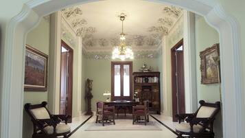 A formal room with a chandelier, two armchairs, a table, and a bookshelf.