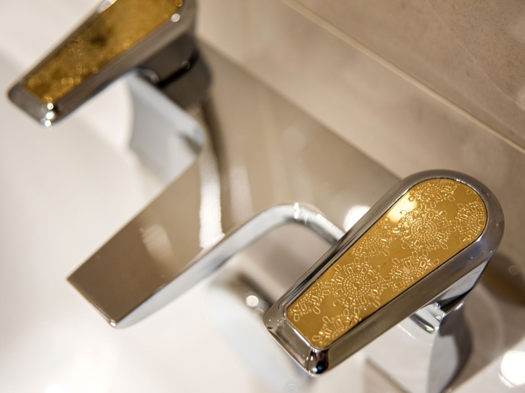A modern bathroom with a chrome faucet and a gold-colored faucet handle.