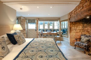 A cozy room with a bed, a table, and chairs, a stone wall, and a window with curtains.