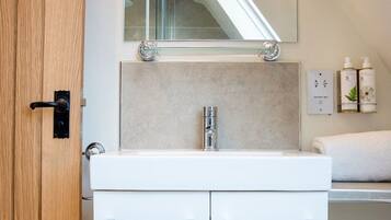 A bathroom with a white sink, a mirror, and a towel rack. There are two bottles on the wall.