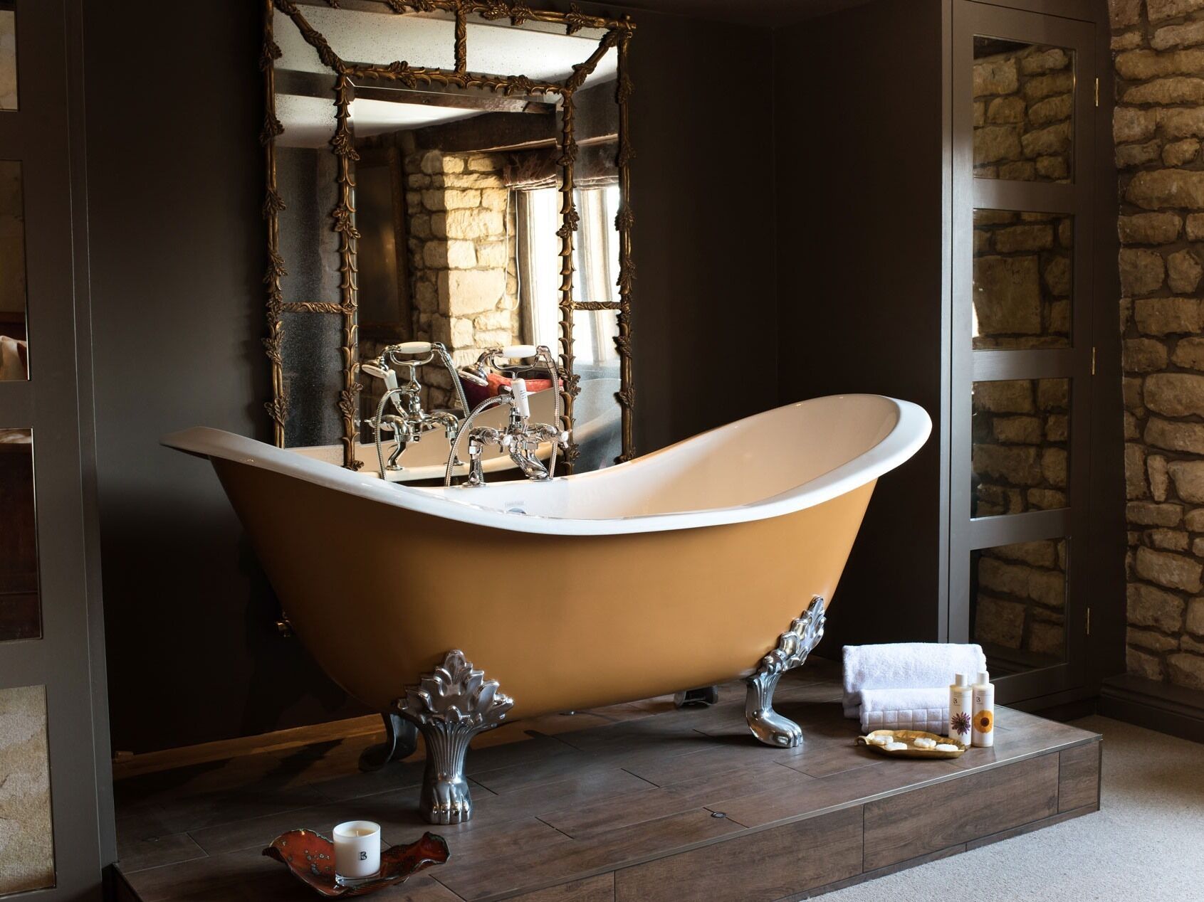 A bathroom with a freestanding bathtub, a stone wall, and a mirror with an ornate frame.