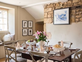 A dining area with a stone wall, framed artwork, and a table set for breakfast.