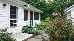 A white house with a front porch, a stone pathway, and various plants. - Farmhouse (Saugatuck)