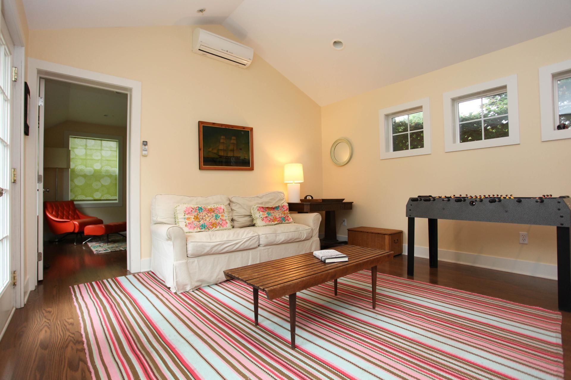 A living room with a sofa, a coffee table, a foosball table, and a window with blinds.