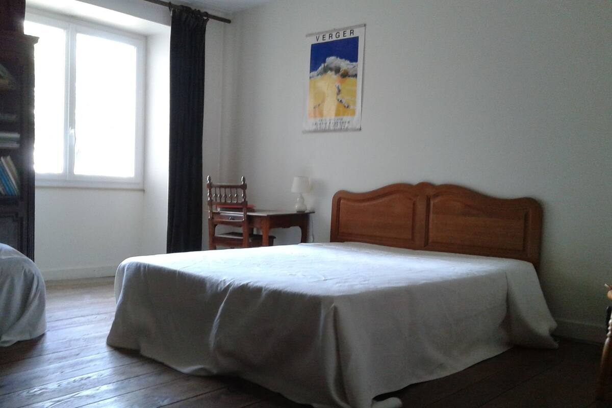 Une chambre à coucher avec un lit en bois, une chaise, un bureau et une fenêtre avec des rideaux.