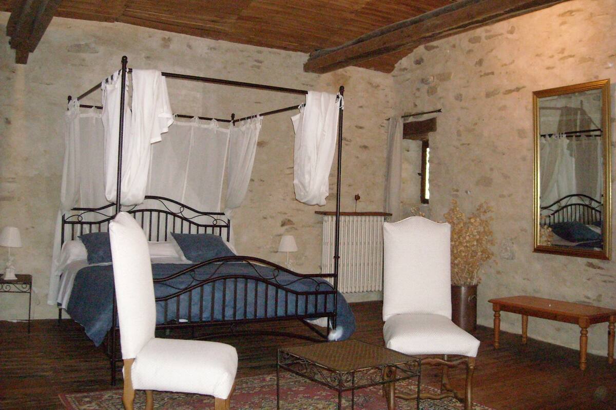 Un lit à baldaquin avec des rideaux blancs, un banc en bois et un miroir au mur.