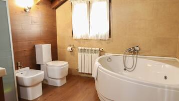 Une salle de bain avec un plancher en bois, une baignoire, deux toilettes et une fenêtre avec des rideaux.