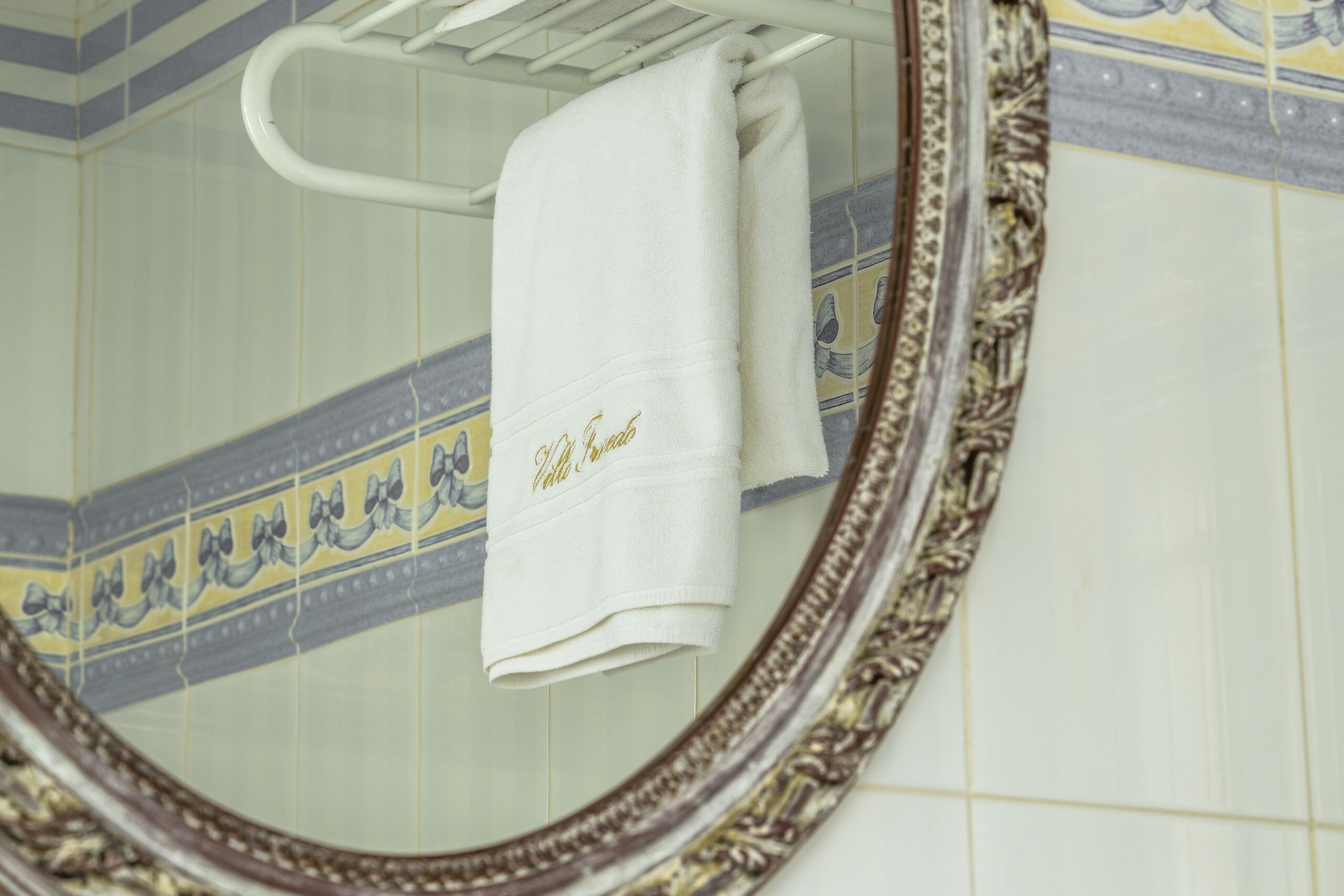 A bathroom with a white towel hanging on a rack, a decorative mirror, and patterned tiles.