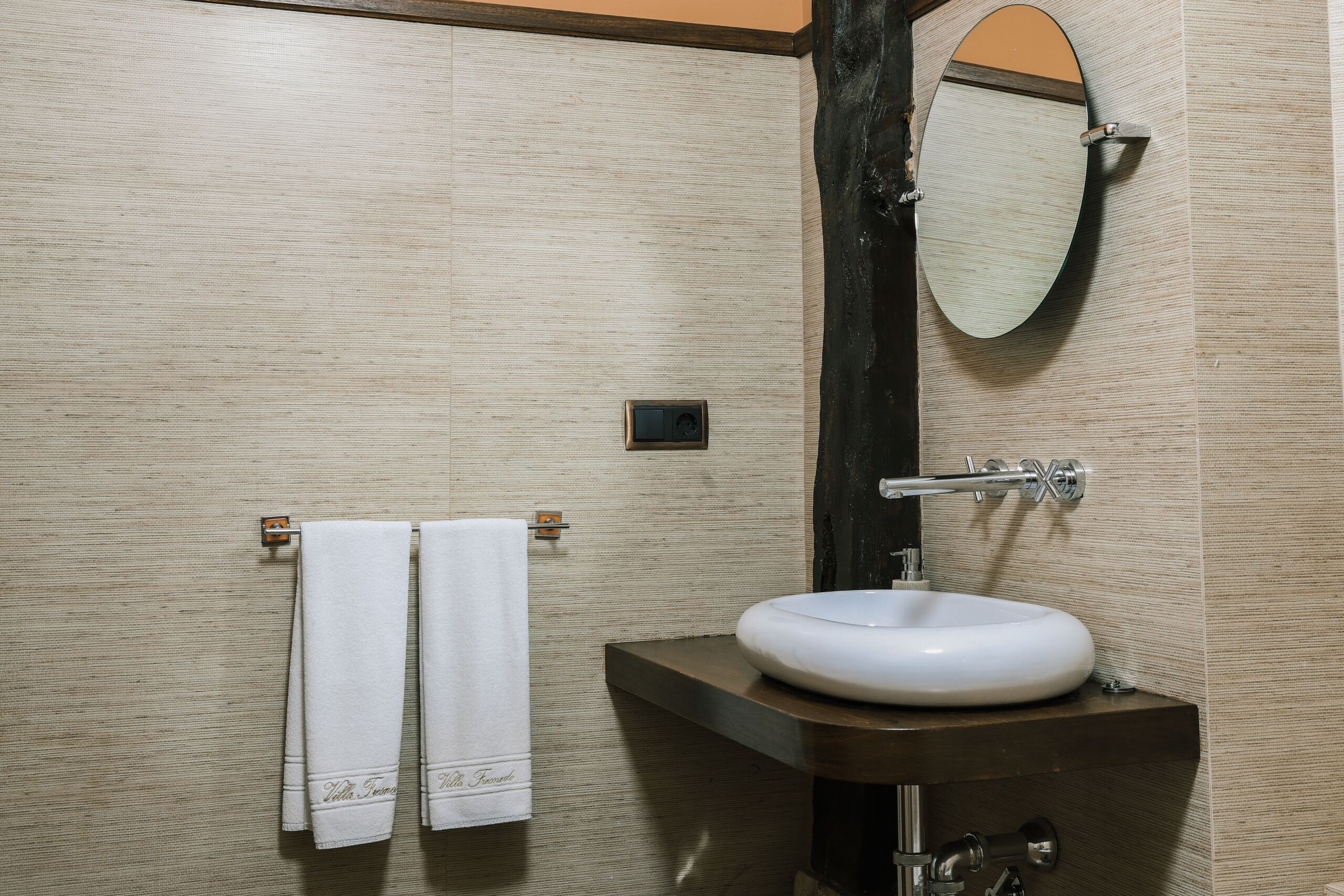 Un baño con un tocador de madera, un lavabo blanco y un espejo. Hay dos toallas blancas colgadas en un perchero.