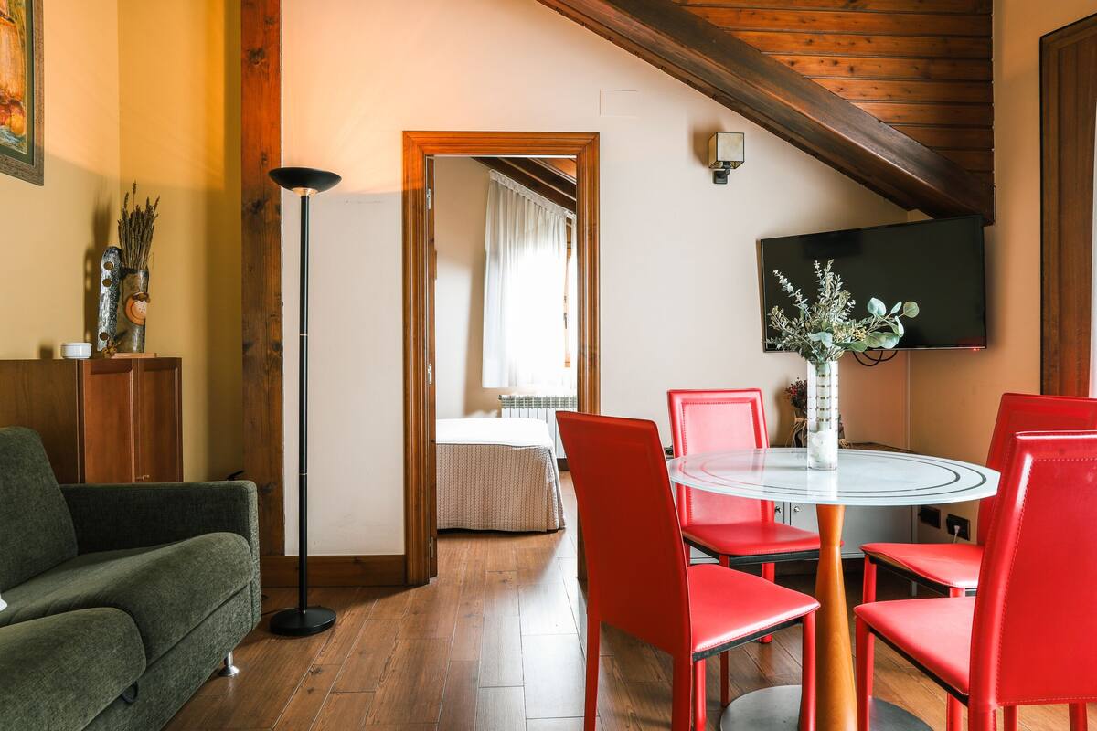 Un coin repas comprenant une table ronde en verre, des chaises rouges, un canapé, une lampe sur pied et un téléviseur fixé au mur.