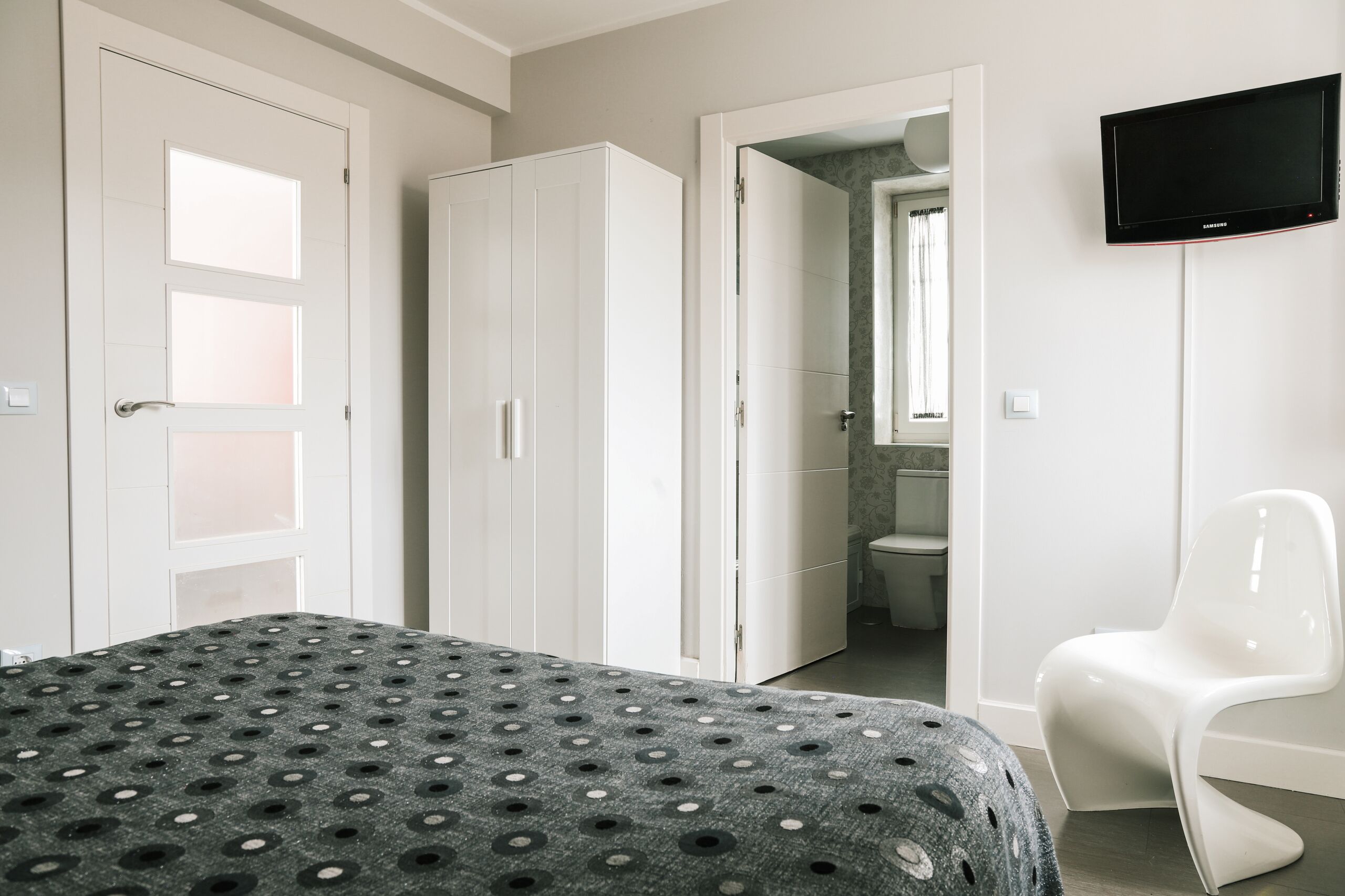 A bedroom with a bed, a wardrobe, a television, and a chair.