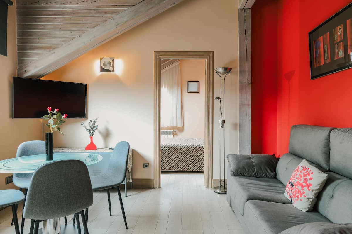 Un salon moderne avec un canapé gris, une table à manger avec des chaises, un téléviseur à écran plat et un mur d’accent rouge.