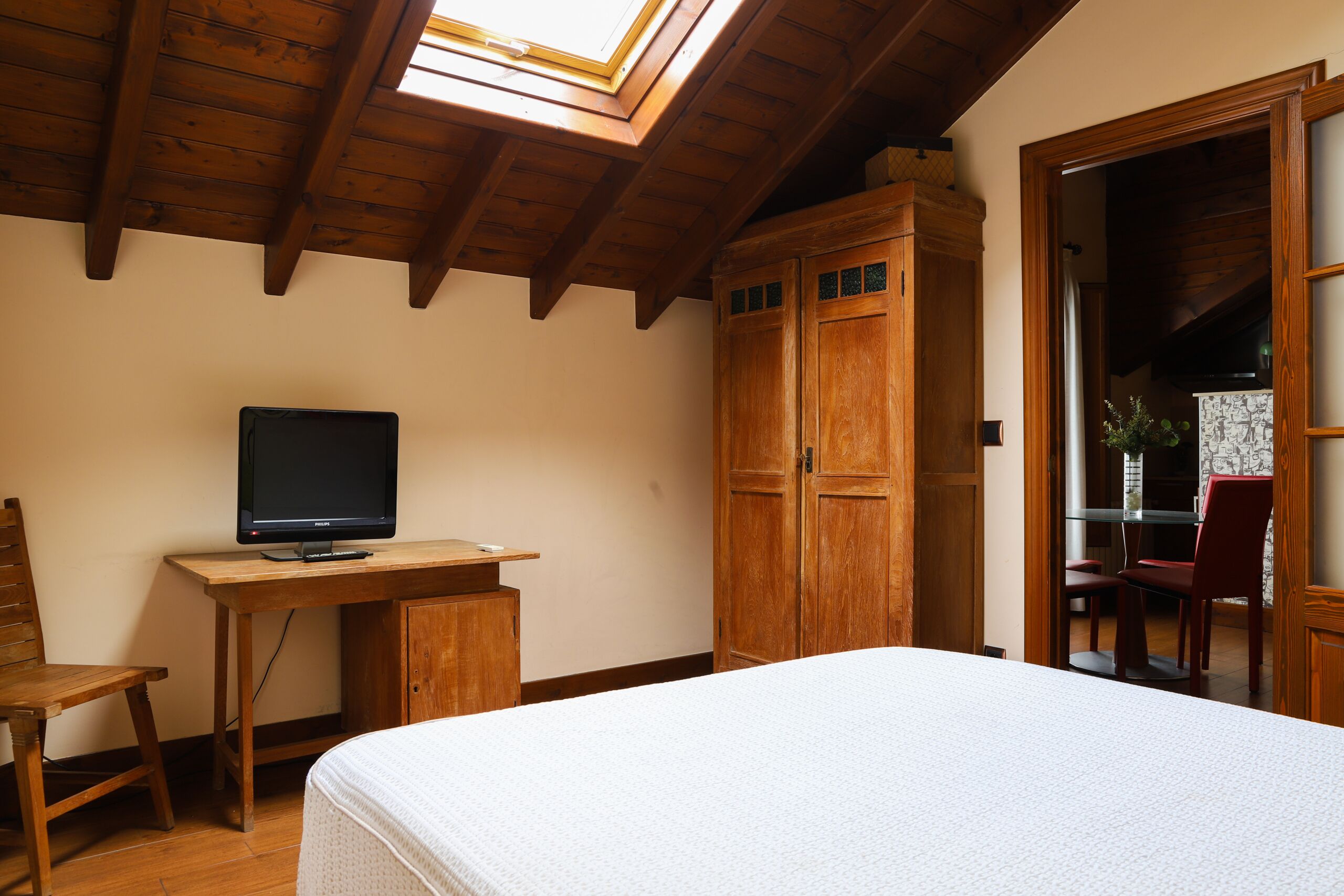 A bedroom with a bed, a desk with a computer, wooden wardrobe, and a skylight.