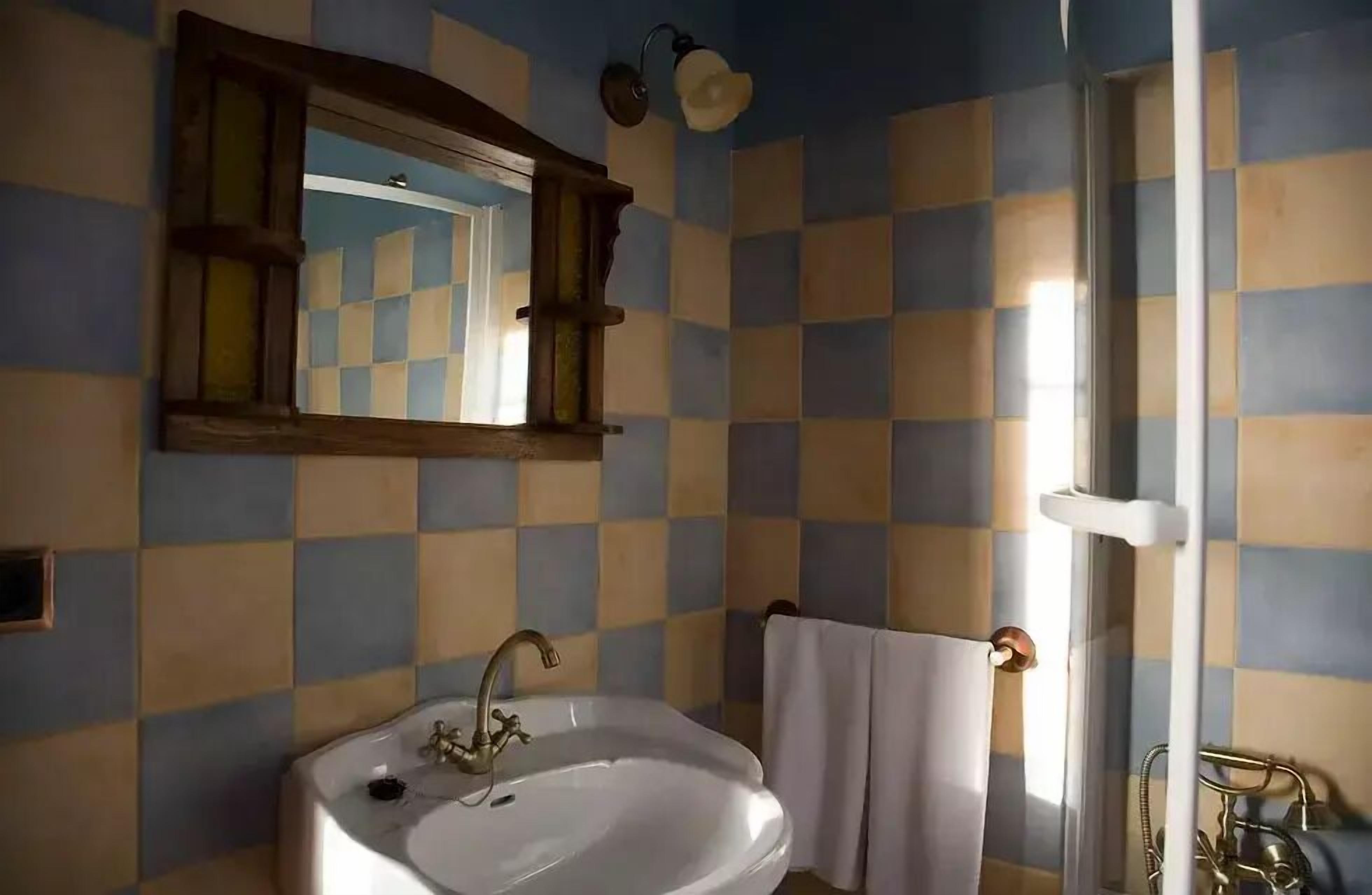 Een badkamer met een betegelde muur in ruitpatroon, een witte wastafel, een spiegel en een handdoekhouder.