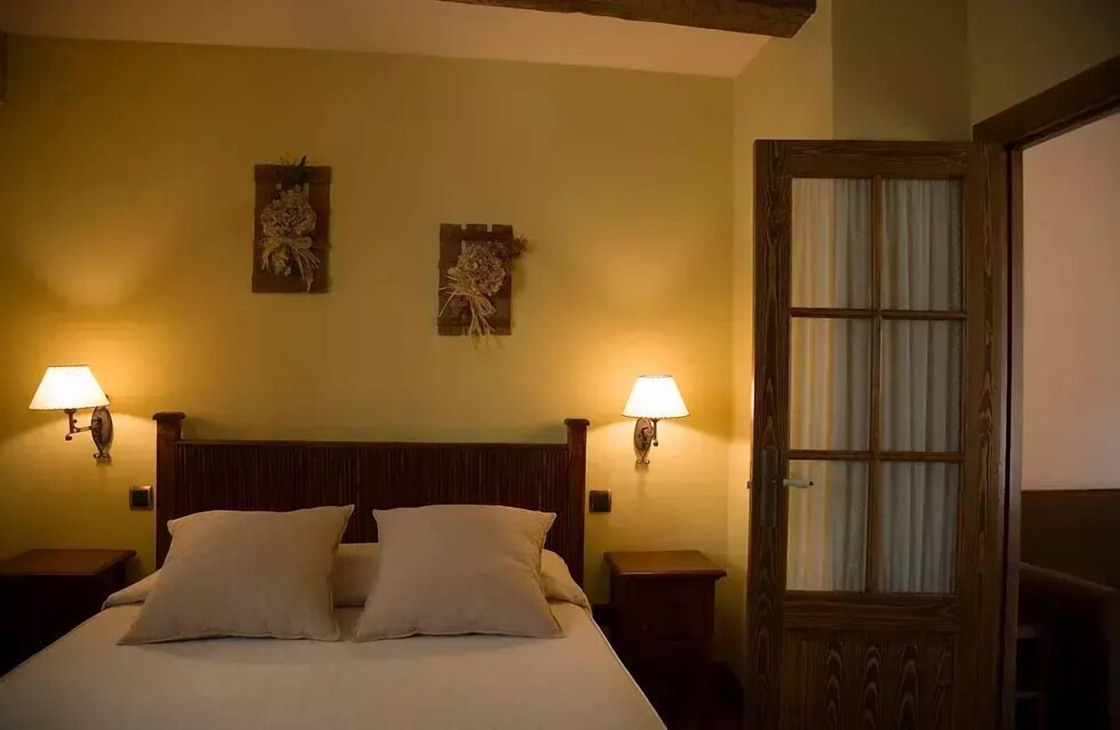 Une chambre d’hôtel avec un lit en bois, deux lampes fixées au mur et une porte avec une fenêtre.