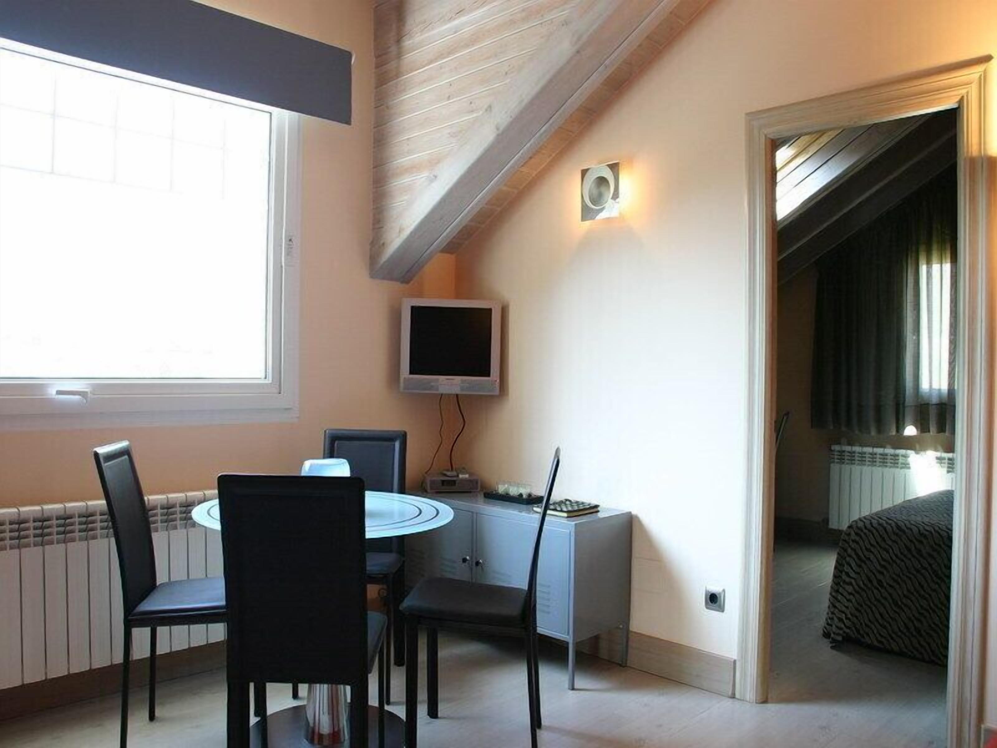 A compact room with a dining table and chairs, a small TV, and a bed with a zebra-patterned cover.