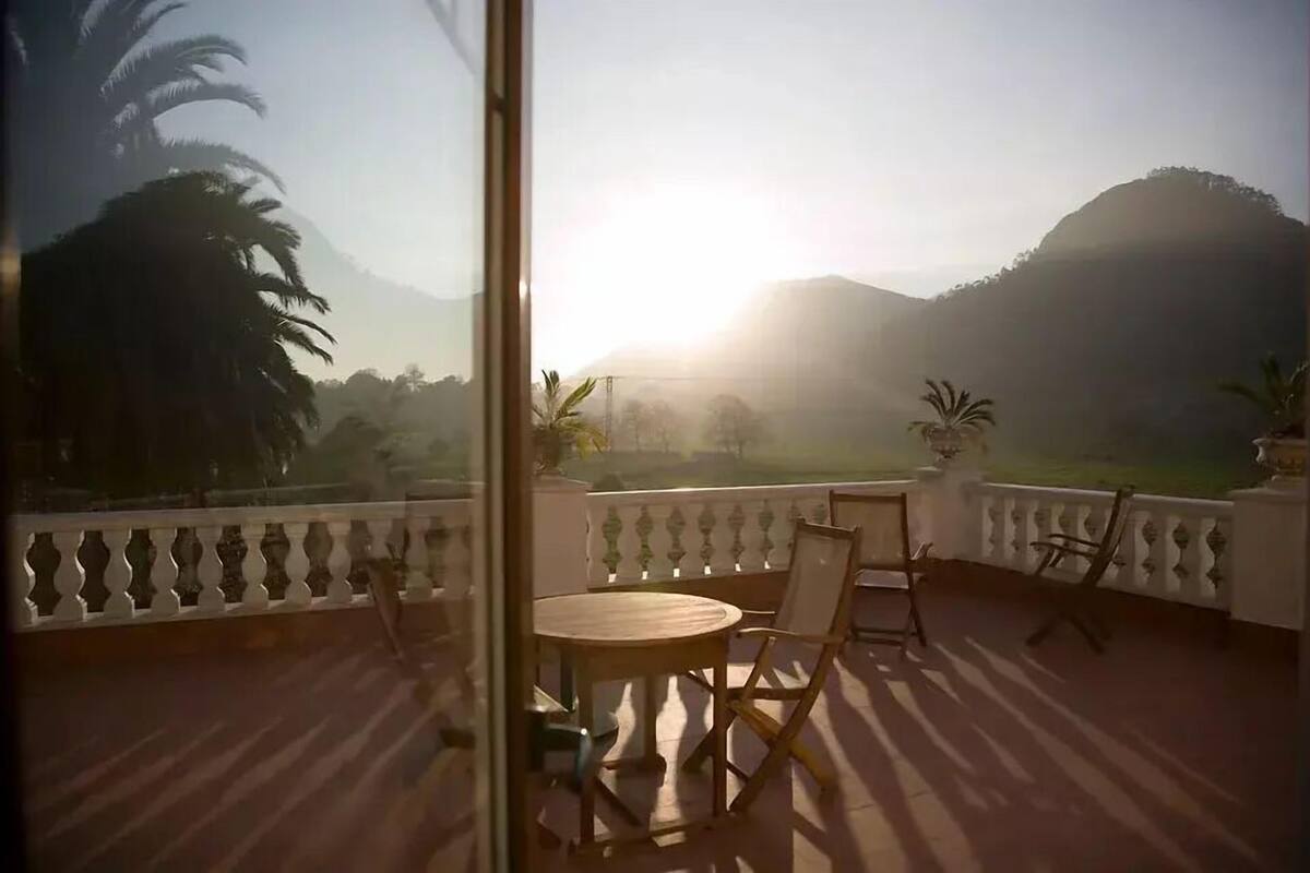 Un balcon avec une table et des chaises, donnant sur un paysage montagneux parsemé de palmiers.