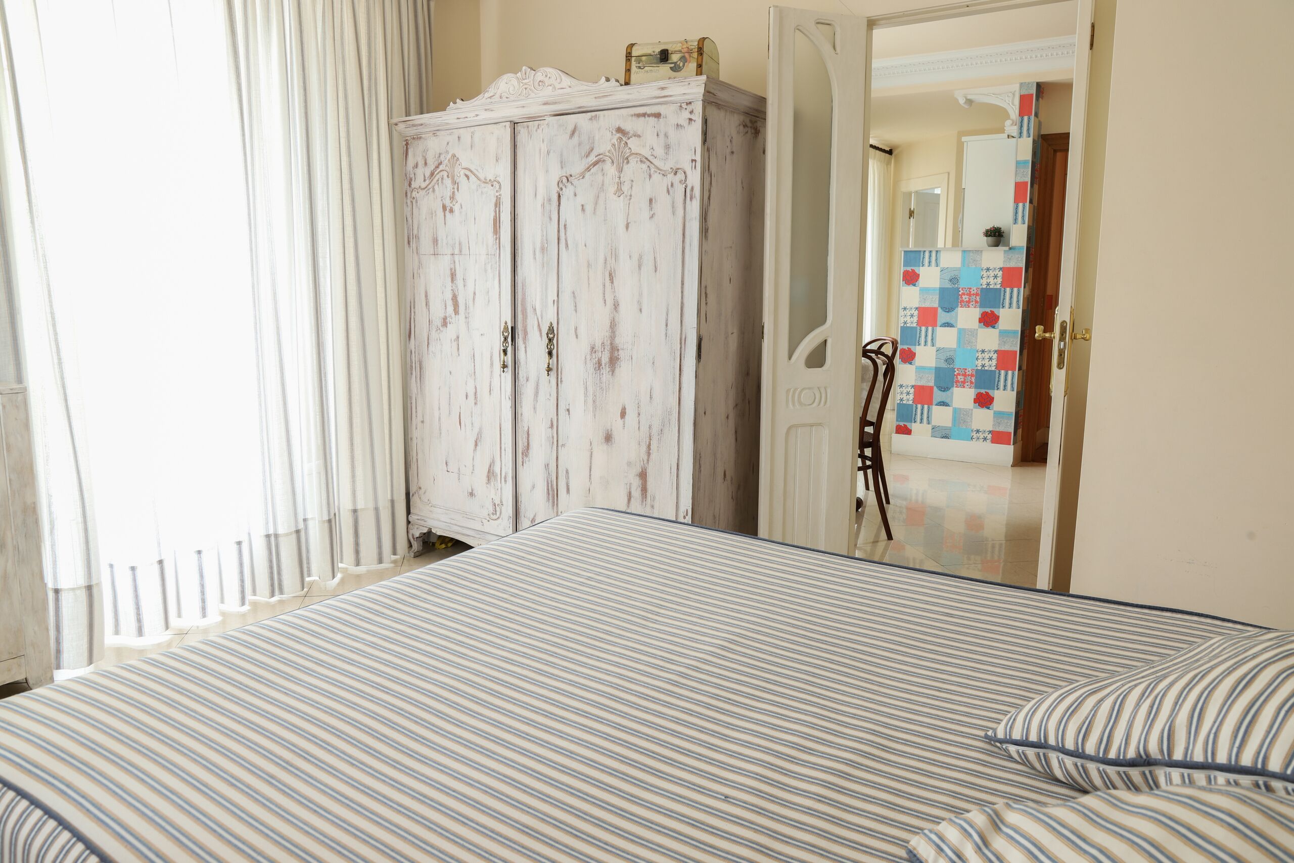 A room with a bed, a wardrobe, and a door leading to another room.