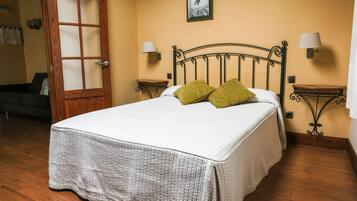 Un dormitorio con cama, dos mesitas de noche, una puerta de madera y una lámpara de pared.