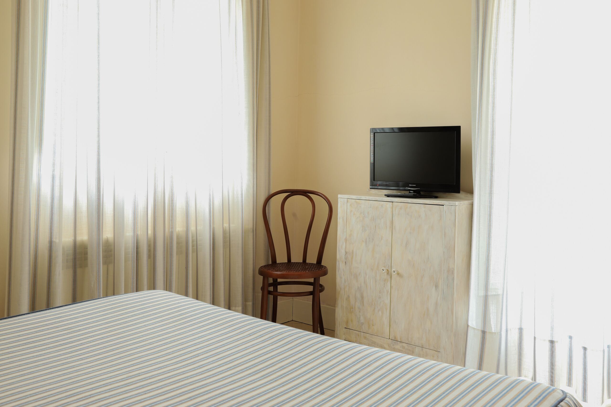 Una habitación de hotel con una cama, un armario de madera con un televisor encima y una silla.