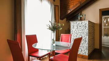 Un coin repas avec une table en verre et des chaises rouges, un vase rempli de fleurs et un buffet à motifs.