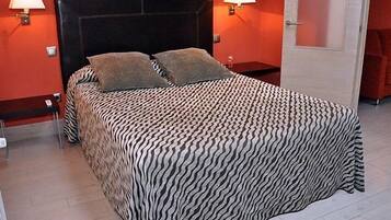 Una cama con colcha de estampado de cebra, dos almohadas y dos lámparas de noche en una habitación con paredes rojas y suelo de madera.