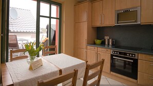 Eine Küche mit Holzausstattung, einer Mikrowelle und einem Backofen. Ein Tisch mit weißem Tischlauf und eine Vase mit Blumen sind ebenfalls vorhanden.
