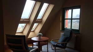 Ein gemütliches Zimmer mit schrägem Dach, einem runden Tisch, zwei Stühlen und einer Heizung.