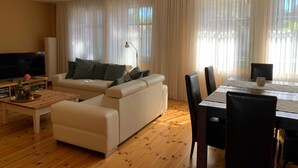 Ein modernes Wohnzimmer mit Sofa, Couchtisch, Fernseher und Essbereich mit Stühlen und Tisch.