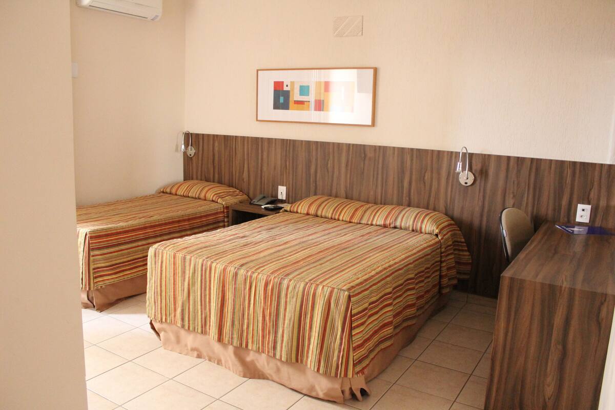 A hotel room with two single beds, a desk, and a chair.