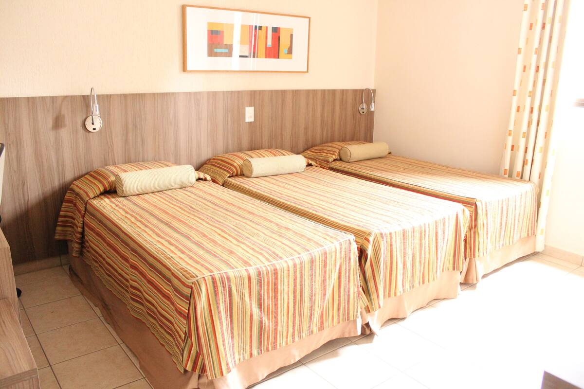 A hotel room with two single beds, a wooden headboard, a framed picture on the wall, and a curtain on the window.