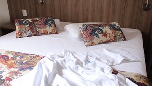 A hotel room with a wooden headboard, two patterned pillows, and a neatly made bed with white linens. - Hotel Riviera (São José do Rio Preto)