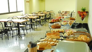 A dining area with tables and chairs, a buffet with various food items, and a fruit display. - Hotel Riviera (São José do Rio Preto)