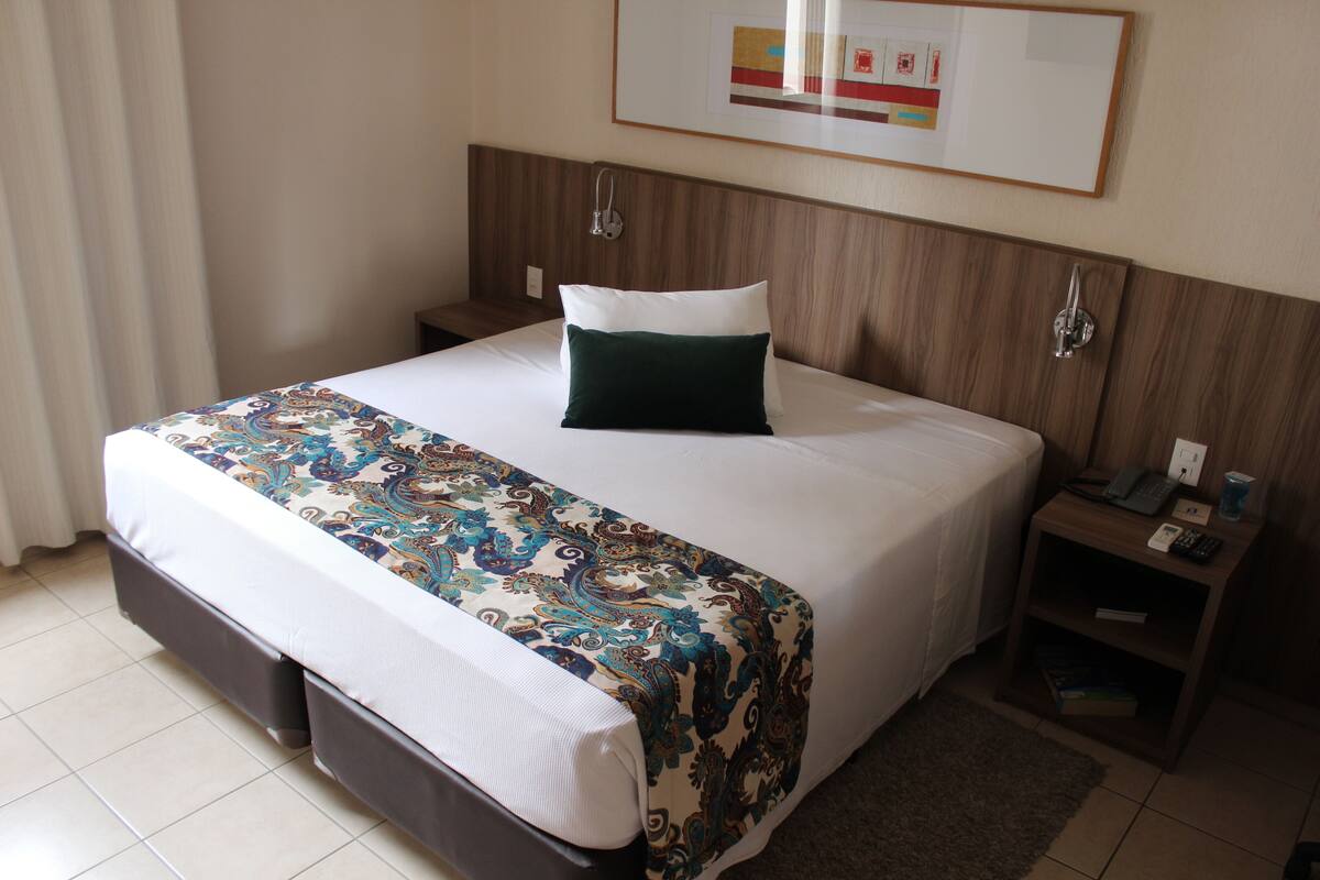 A hotel room with a bed, a nightstand, a telephone, and a framed picture on the wall.
