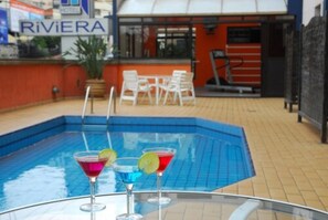 Uima-allas, jossa on kolme värikästä juomaa, kyltti, jossa lukee ”RIVIERA”, ja ulkotila, jossa on istuimia.