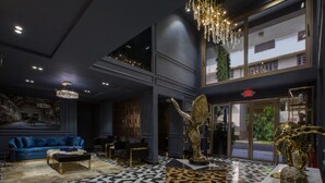 Um hall com piso xadrez, um sofá azul, uma estátua dourada e um candelabro.