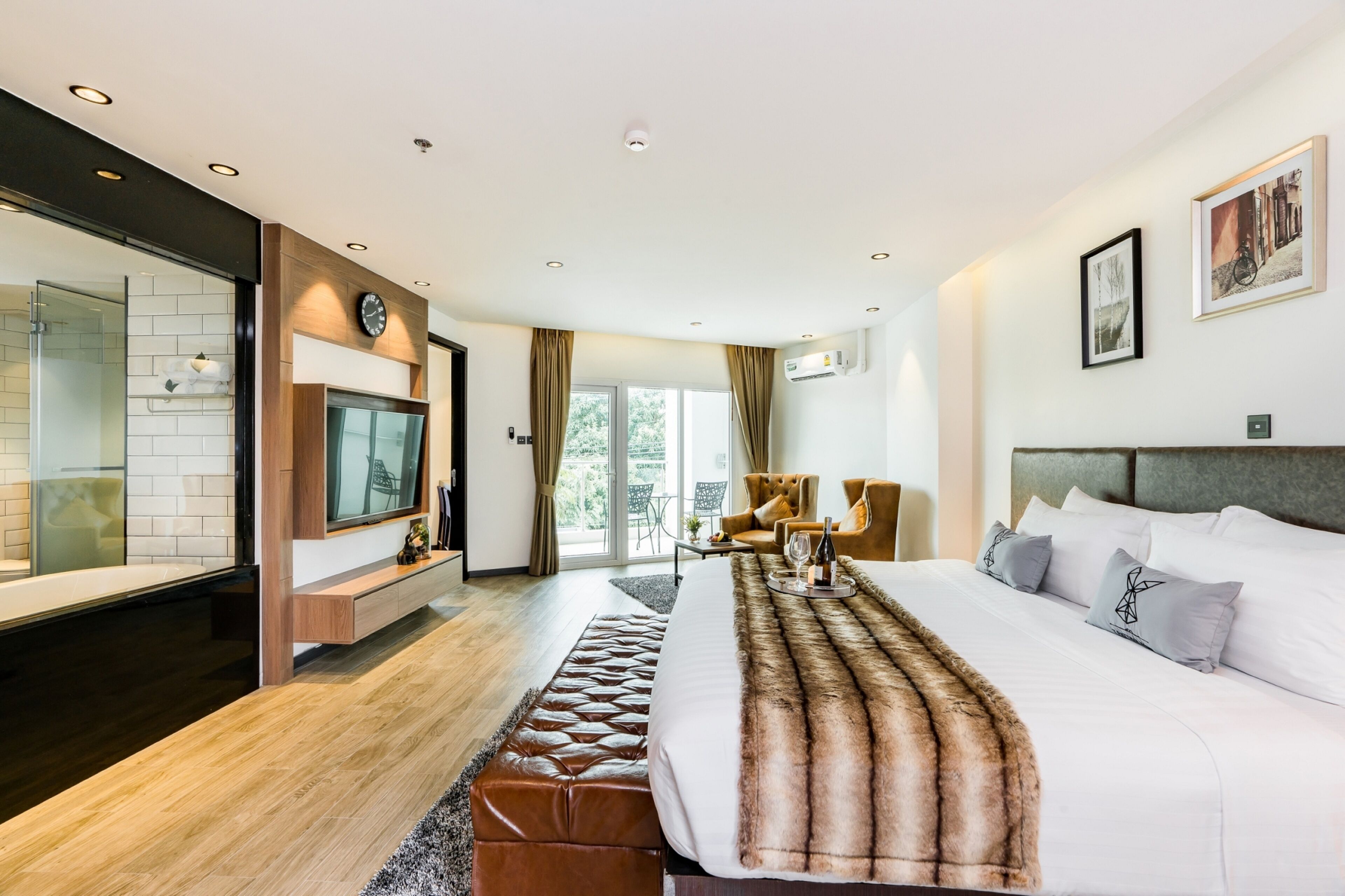 Ein modernes Hotelzimmer mit einem großen Bett, einem Fernseher, einer Sitzecke mit Tisch und Stühlen sowie Blick ins Freie.