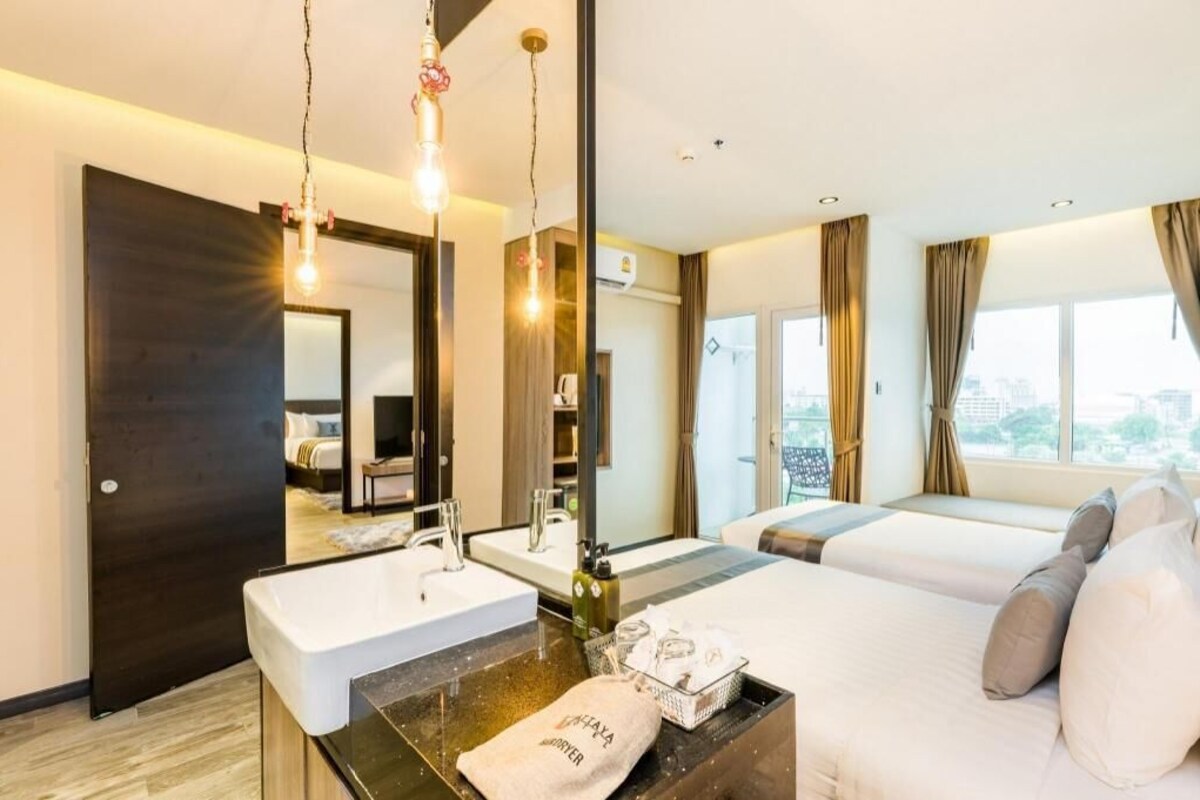 A hotel room with a large bed, a separate bathroom with a sink, a mirror, and a view of the city.