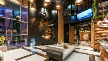 A modern lobby with a geometric light fixture, a seating area, and a large TV screen.
