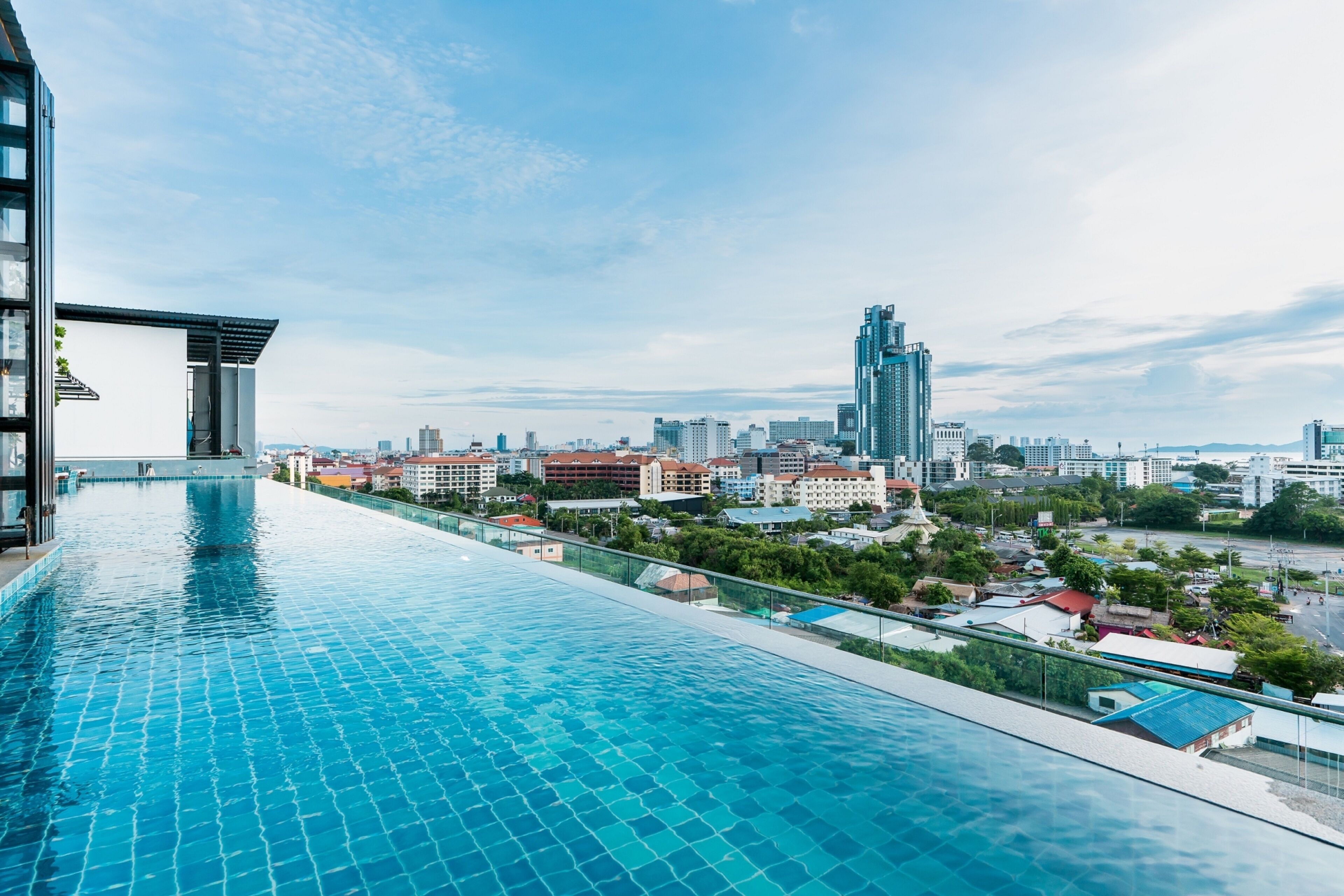 Une piscine à débordement située sur le toit, offrant une vue panoramique sur la ville, avec des bâtiments modernes et un ciel dégagé.