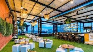 Eine Dachterrasse mit weißen Sitzgelegenheiten, hängenden Lichtern und Blick auf die Stadt.