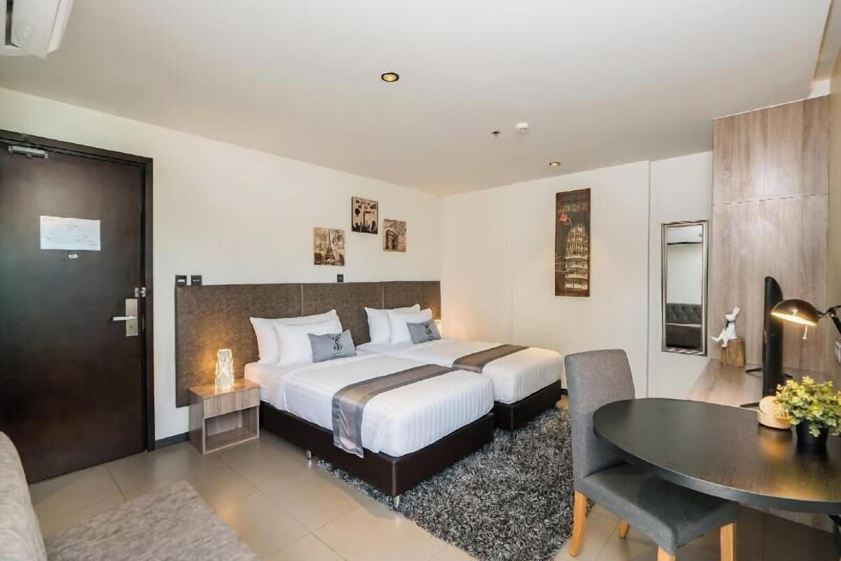 A hotel room with two beds, a desk, a chair, a mirror, and artwork on the walls.