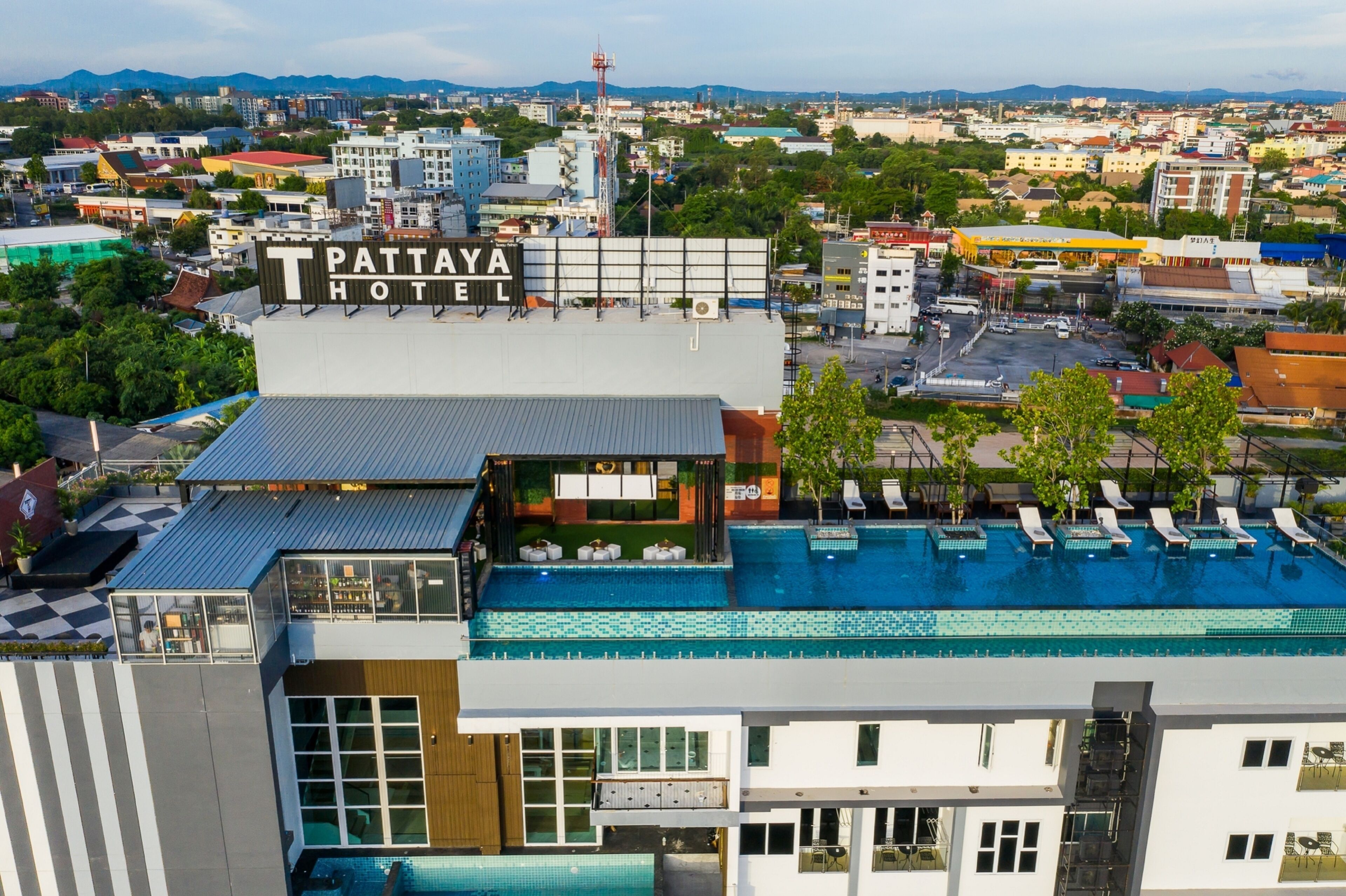 Un hôtel doté d’une piscine sur le toit, d’une enseigne indiquant « Hôtel de Pattaya », et offrant une vue sur le paysage urbain en arrière-plan.