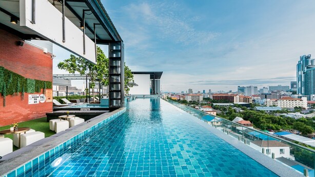 Ein langer, schmaler Infinity-Pool mit Blick auf die Stadtlandschaft, moderne Architektur und Sitzmöglichkeiten im Freien.