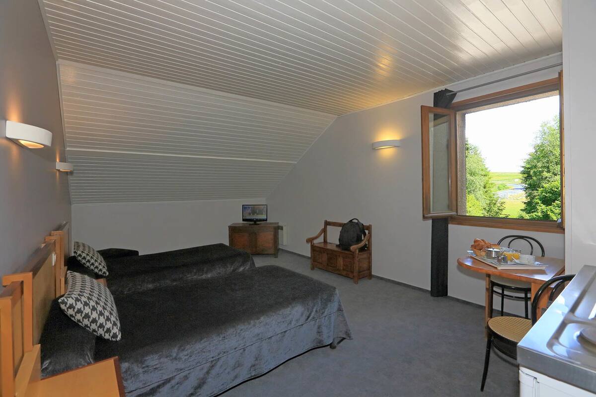 Une chambre à coucher comprenant un lit, une chaise, une petite table avec un plateau, et une fenêtre donnant sur un paysage verdoyant.