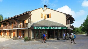 Un hôtel appelé « HÔTEL LE BASTIDE », doté d’un balcon, d’un espace extérieur aménagé et d’une façade en pierre.