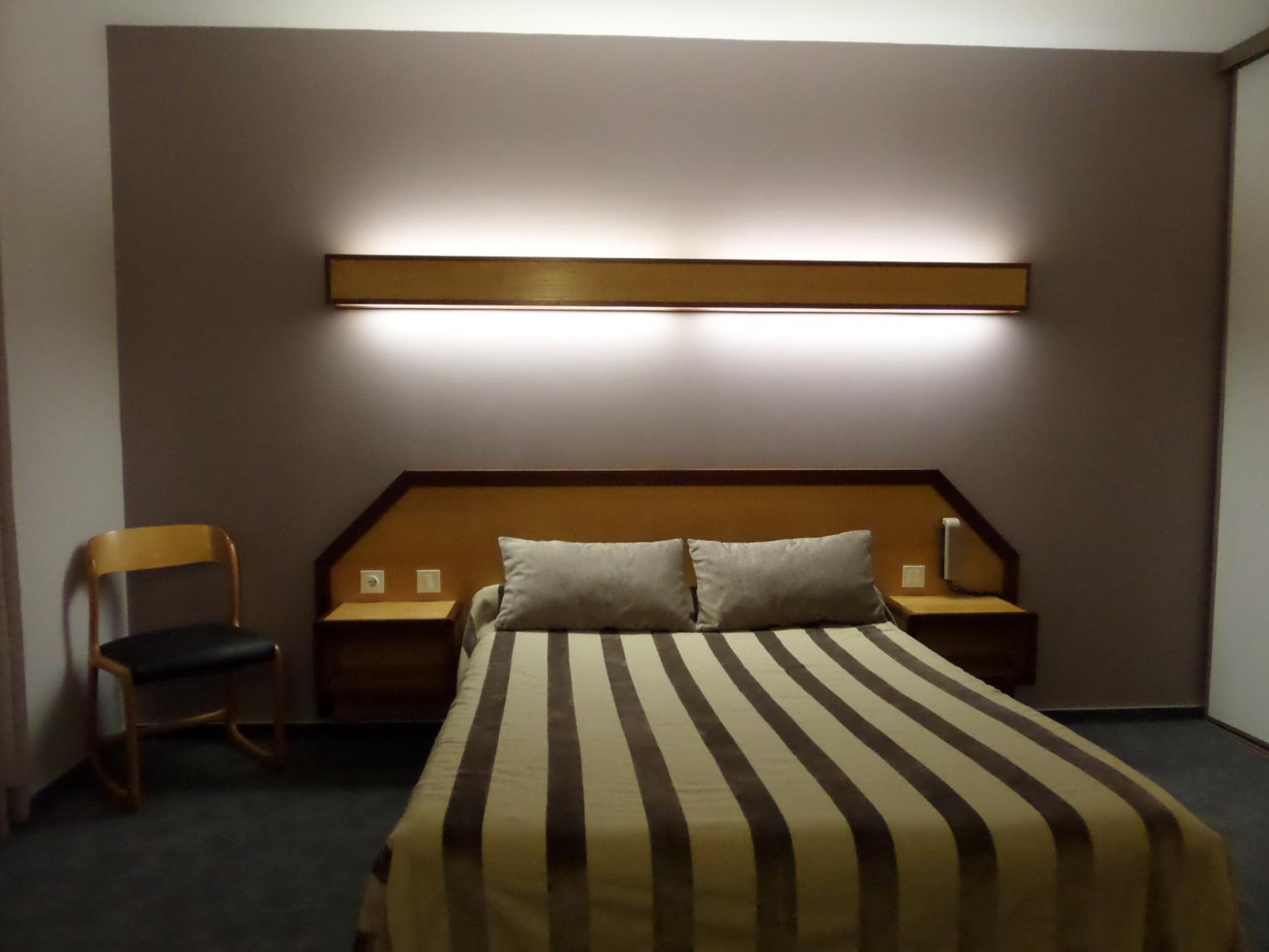 Ett hotellrum med en säng, två sängbord, en stol och en väggmonterad lampa.
