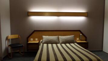 Ett hotellrum med en säng, två sängbord, en stol och en väggmonterad lampa.