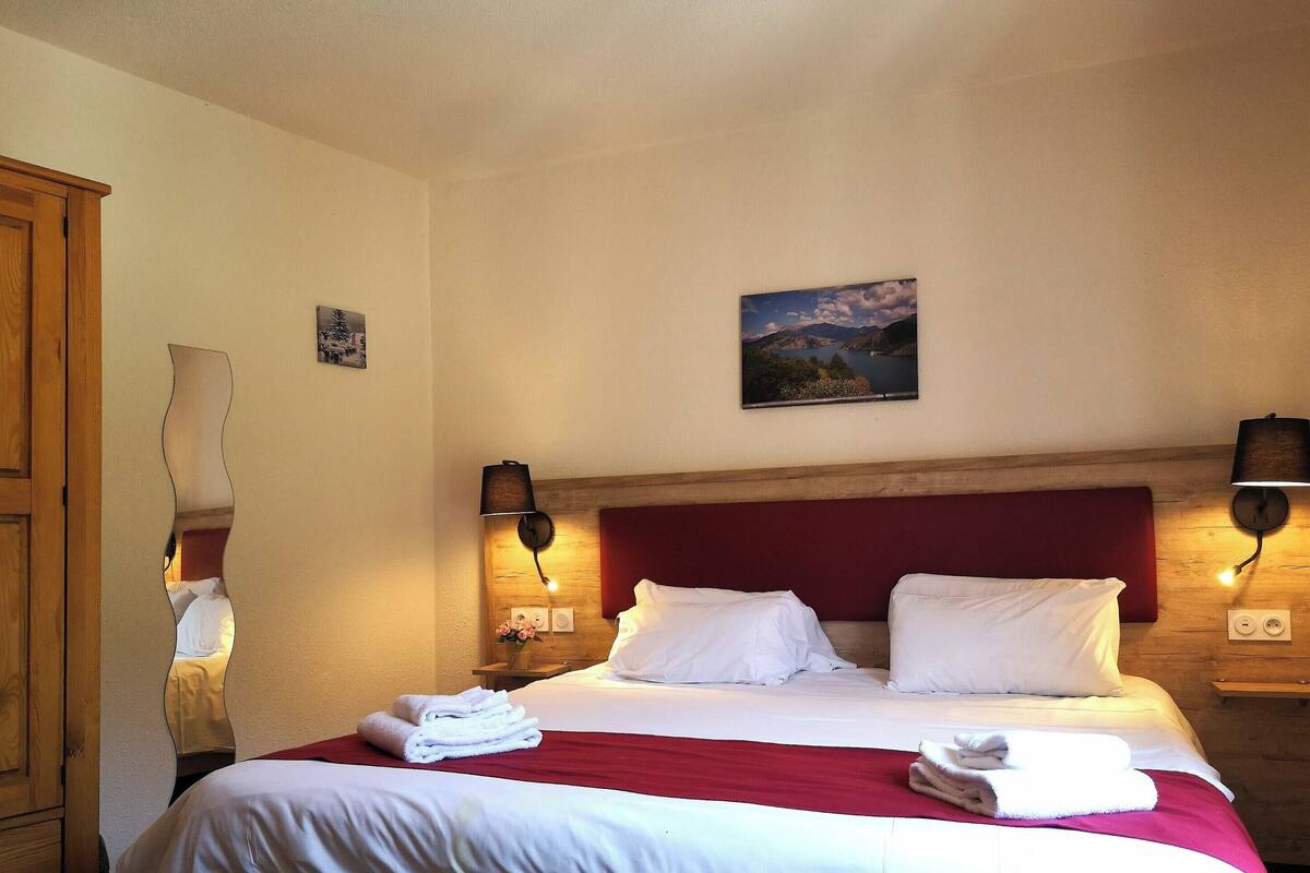A neatly made bed with white linens, a red headboard, and two wall-mounted lamps.